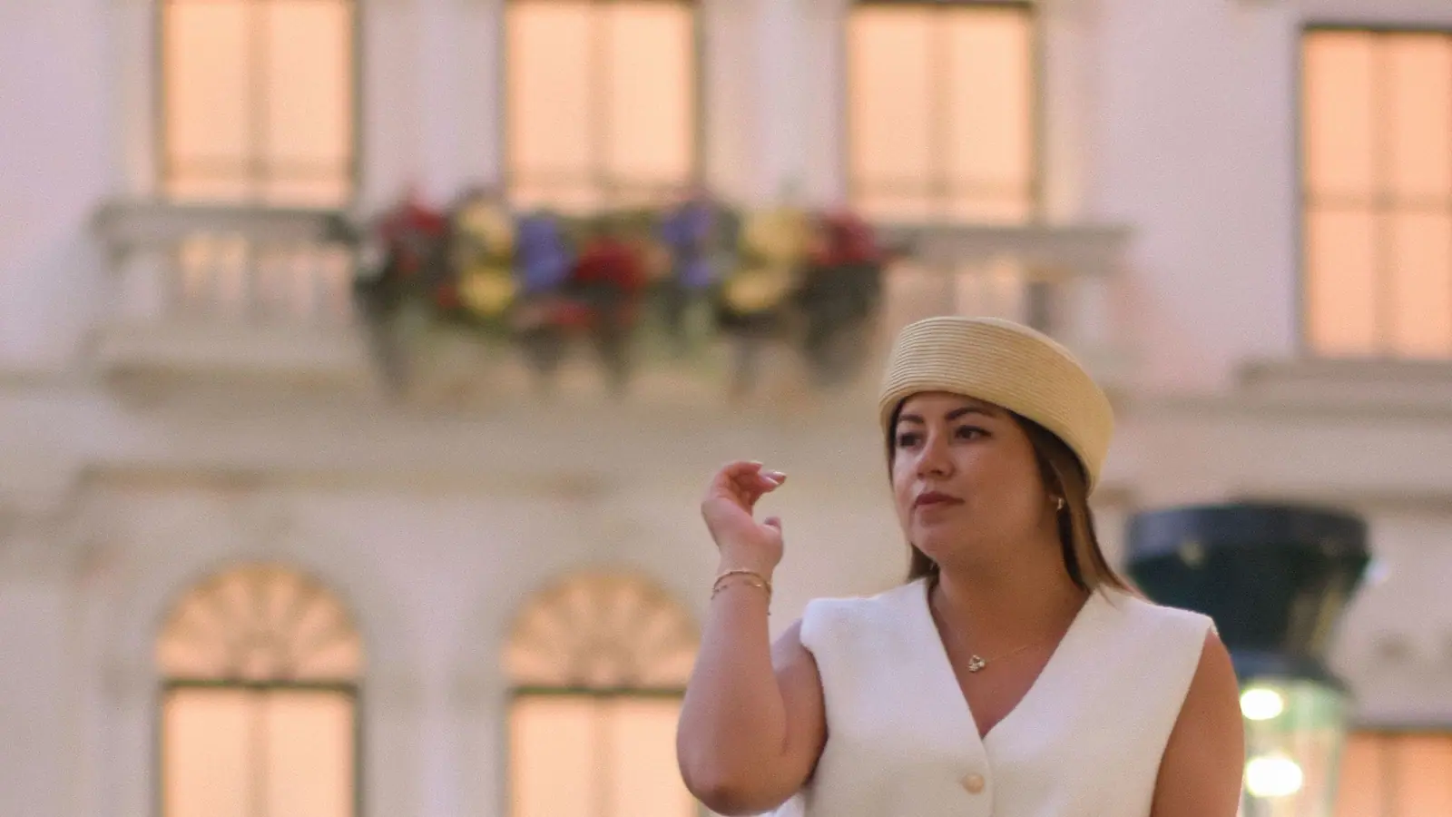 Alejandra Ubaldo in a white vest and straw beret on a stone balcony at golden hour