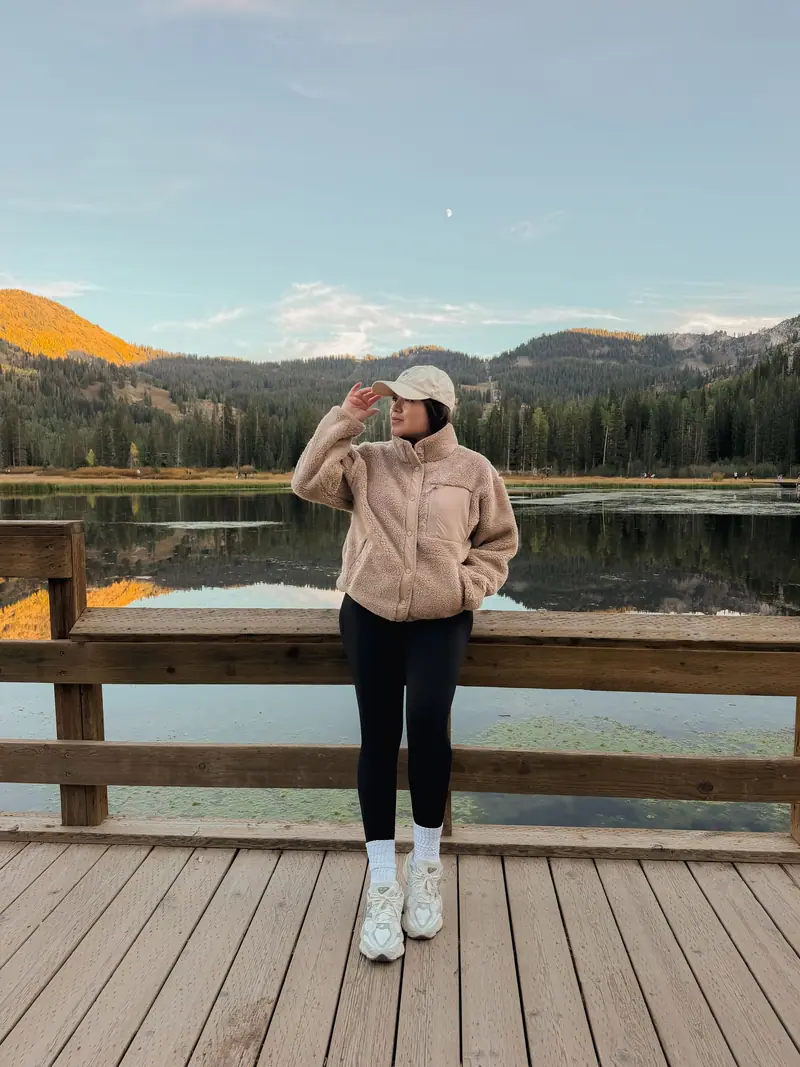Cream sherpa fleece and cap on a wooden dock above a mountain lake in autumn