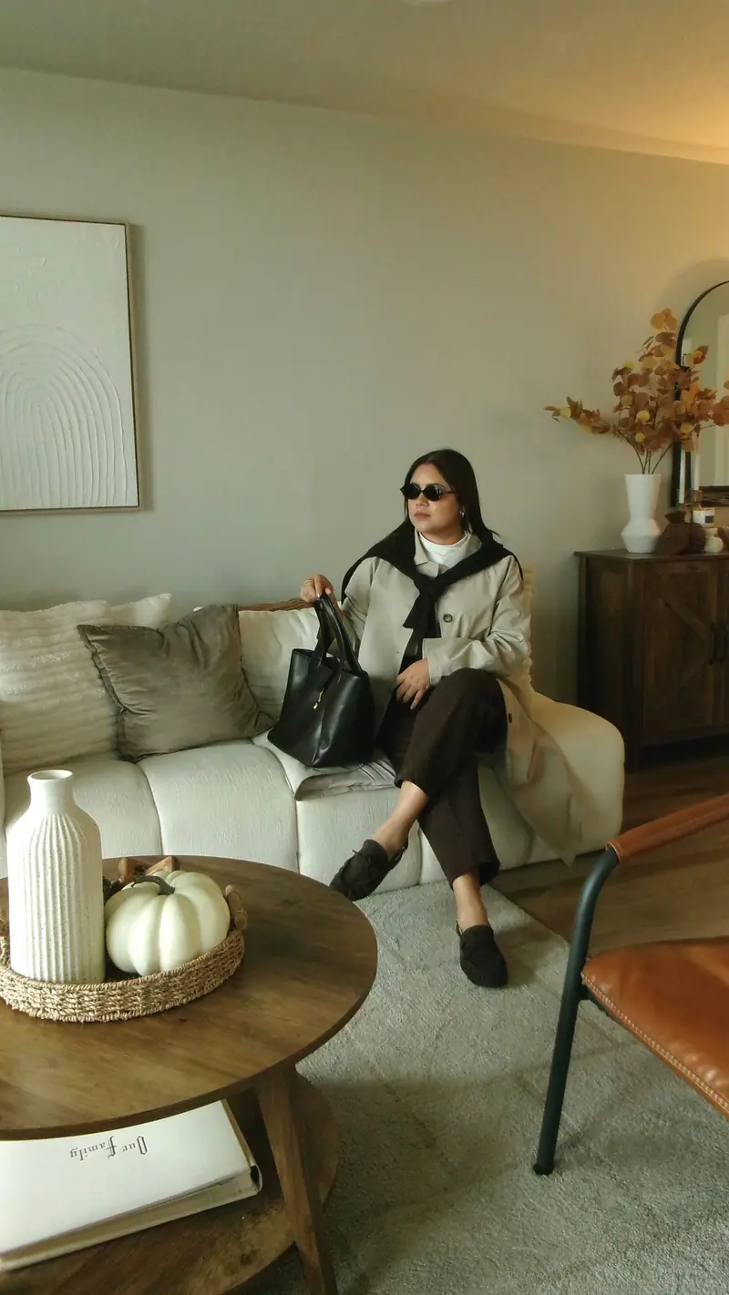 Neutral trench coat styling in a warm living room with fall decor and a white pumpkin