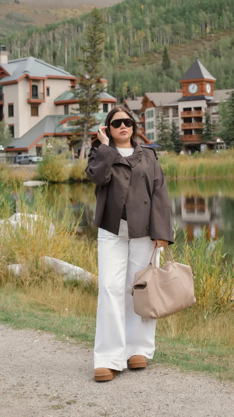 Cropped brown jacket and wide white trousers beside a mountain-village pond