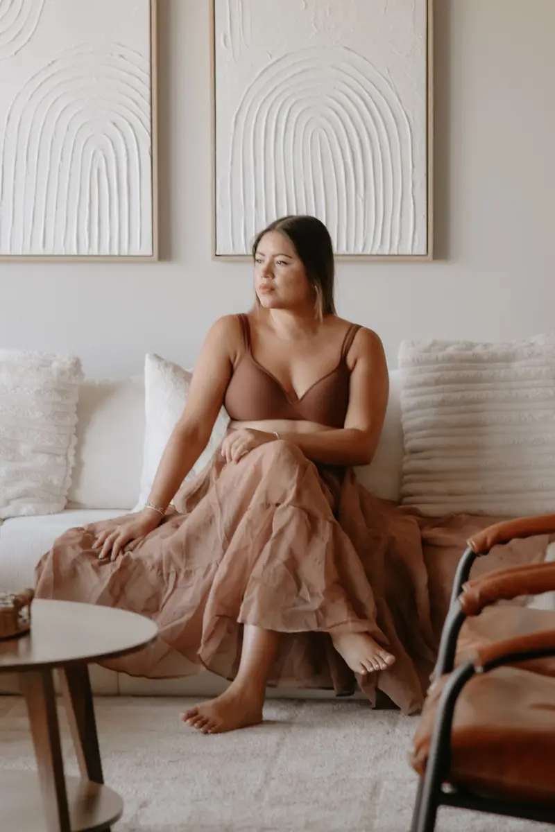 Alejandra seated on a cream sofa in a flowing terracotta skirt in front of arch wall art